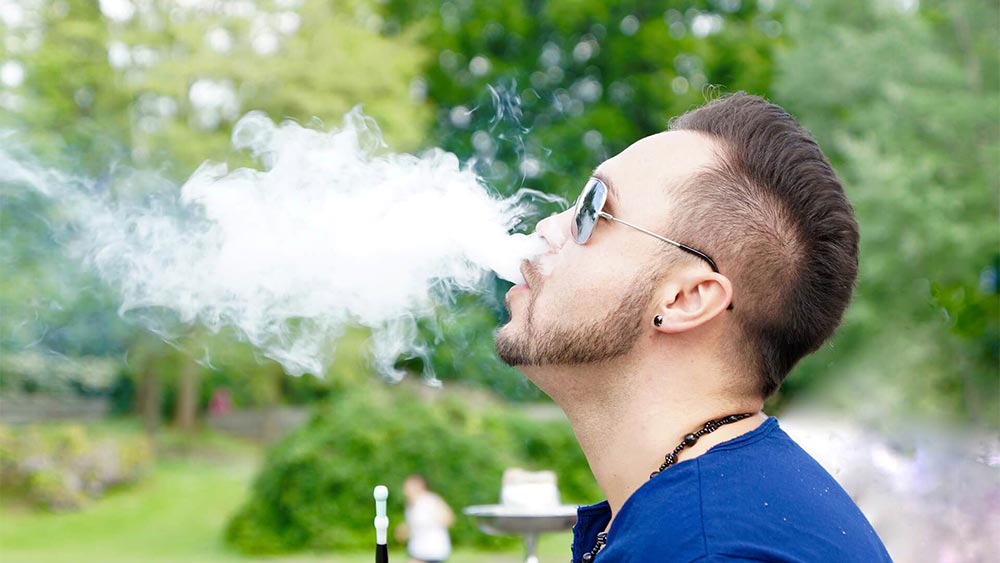 barbat intr-un parc care fumeaza dintr-o narghilea