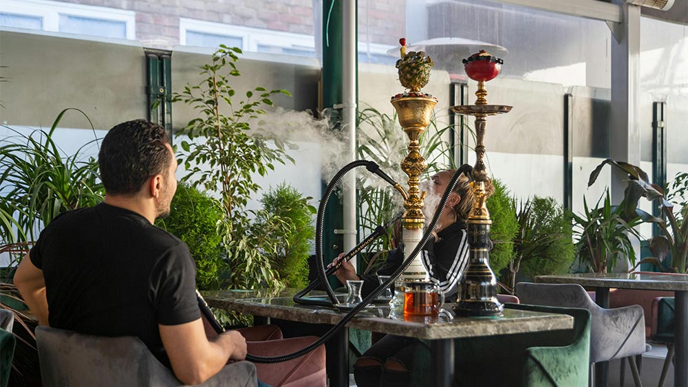 2 oameni la o masa fumand din narghilele
