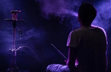 Persoana care fumeaza o narghilea intr-o camera intunecata