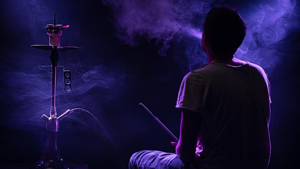 Persoana care fumeaza o narghilea intr-o camera intunecata